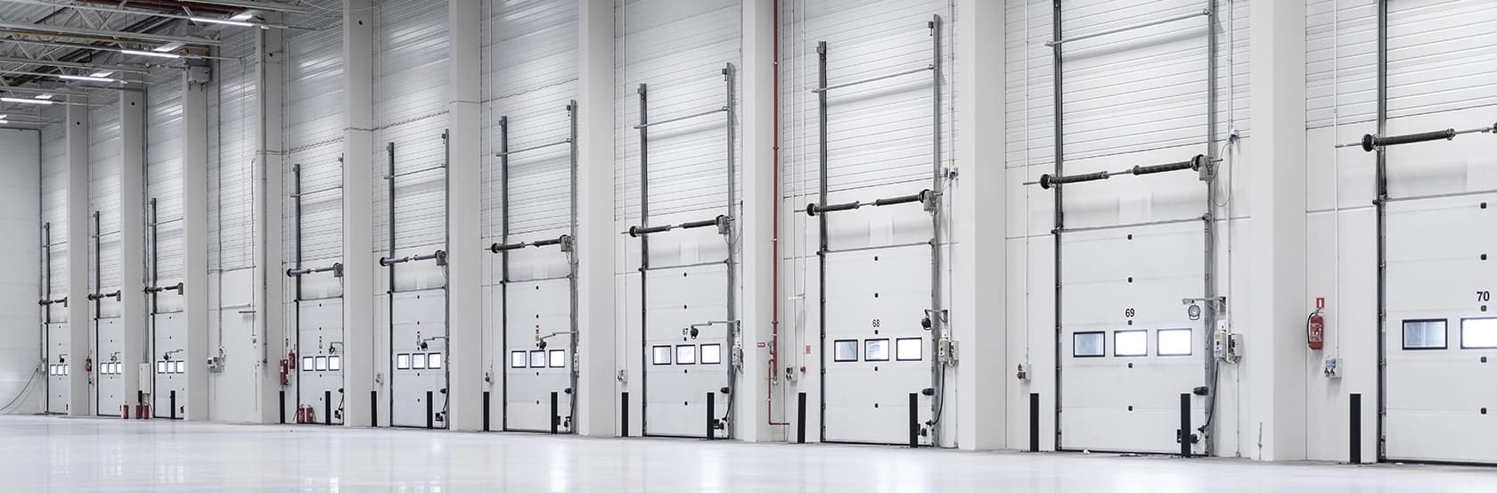 Rząd segmentowych bram przemysłowych w dużej hali produkcyjnej lub magazynie